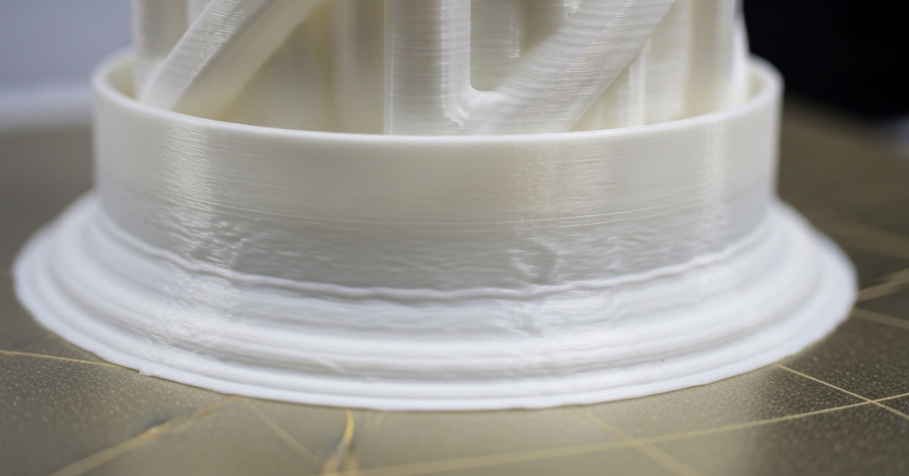 Close-up of a Nylon 3D print showing edge lifting and base warping on the build plate, demonstrating poor adhesion and thermal stress.