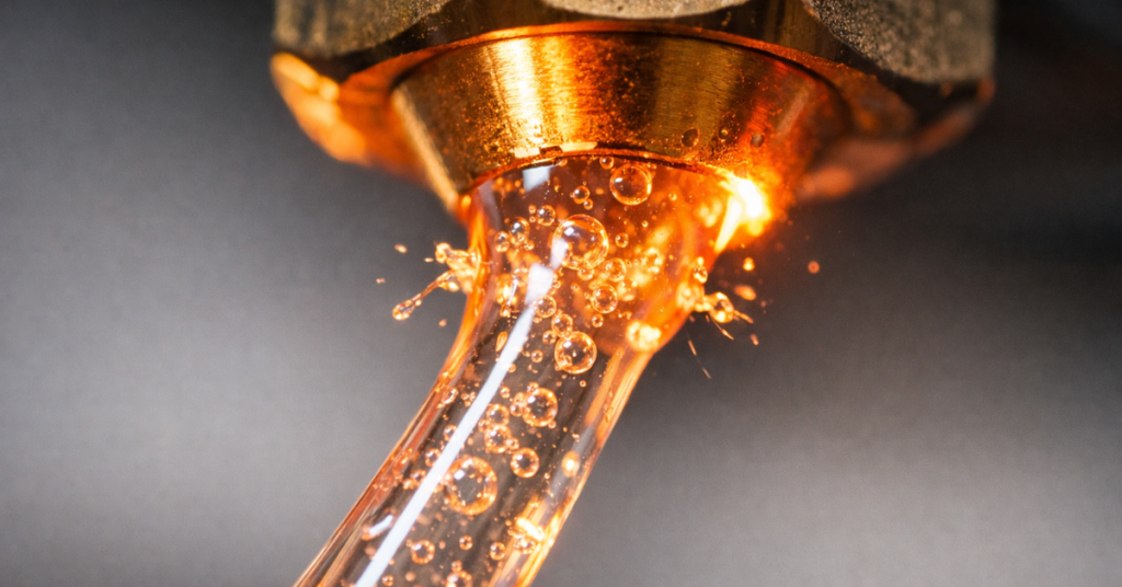 Macro close-up of molten filament extruding from a 3D printer nozzle with visible air bubbles, showing a clear sign of moisture contamination.