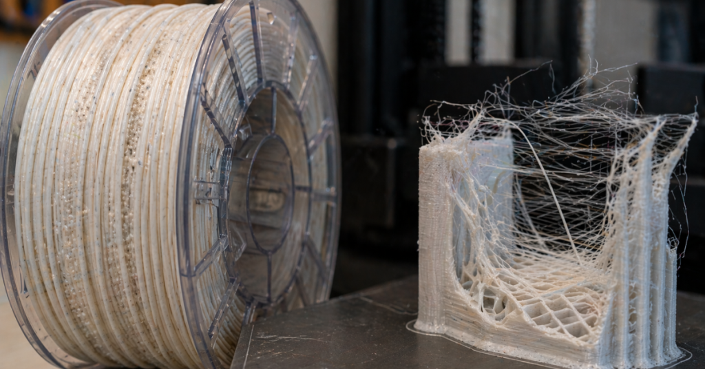 Moisture-exposed filament spool next to a failed 3D print showing severe stringing and poor layer quality
